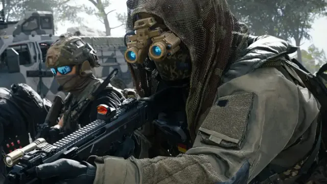 Three operators moving through a forest beside an armoured vehicle